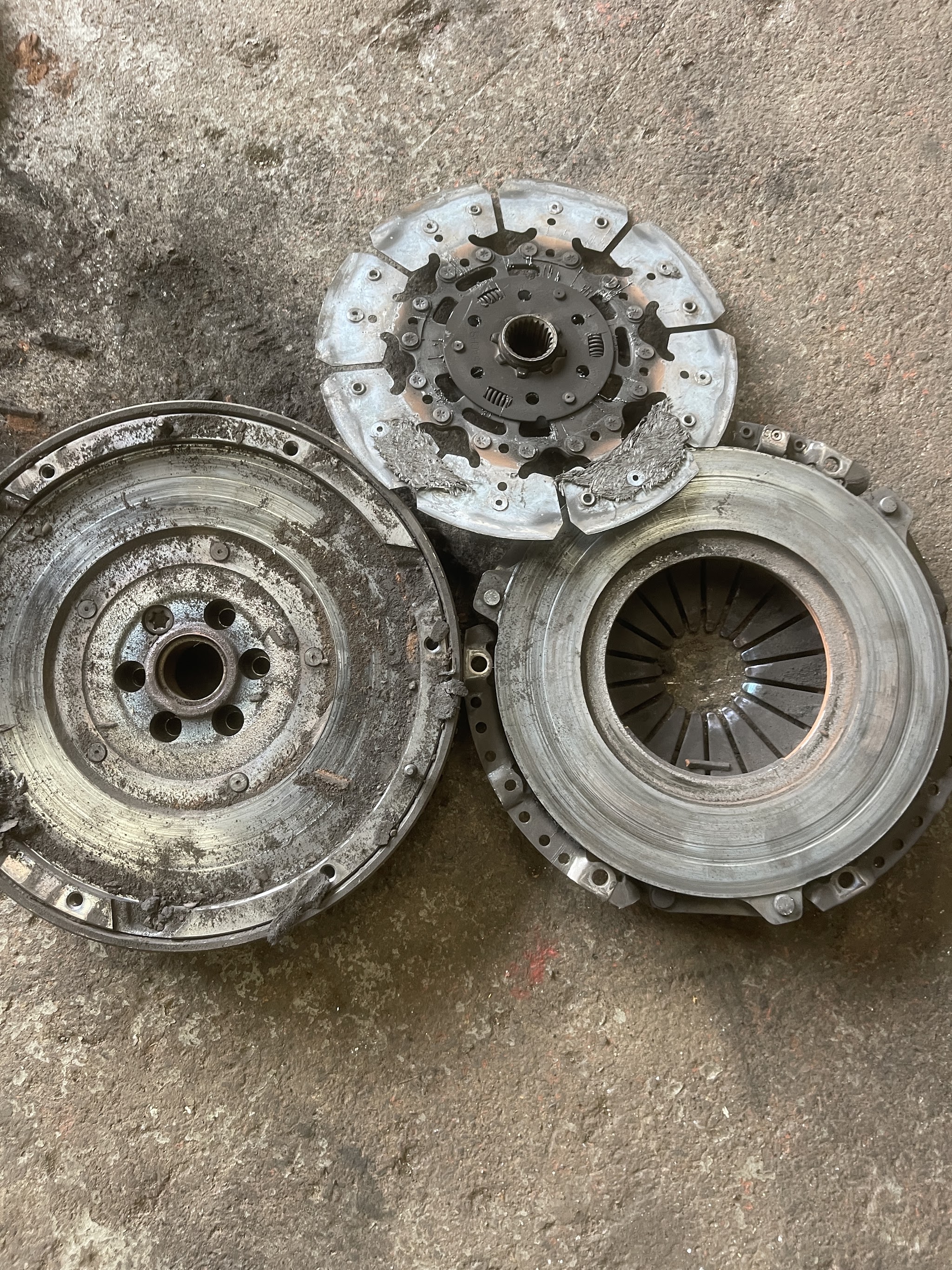 A worn out clutch plate, pressure plate and flywheel taken off a car, lying on the workshop floor
