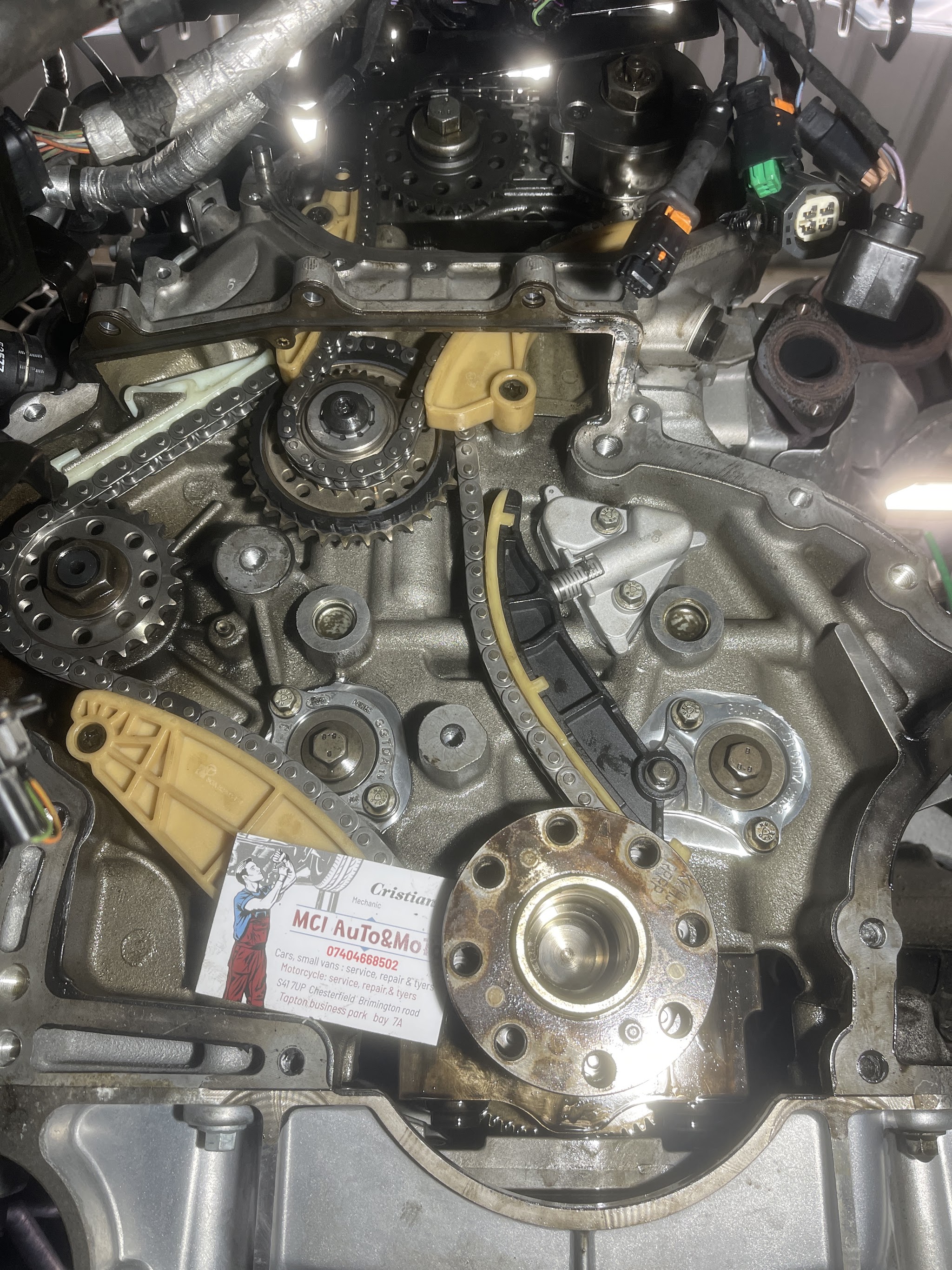 An engine with its timing chain exposed and Cristian's MCI AuTo&MoTo business card resting on it
