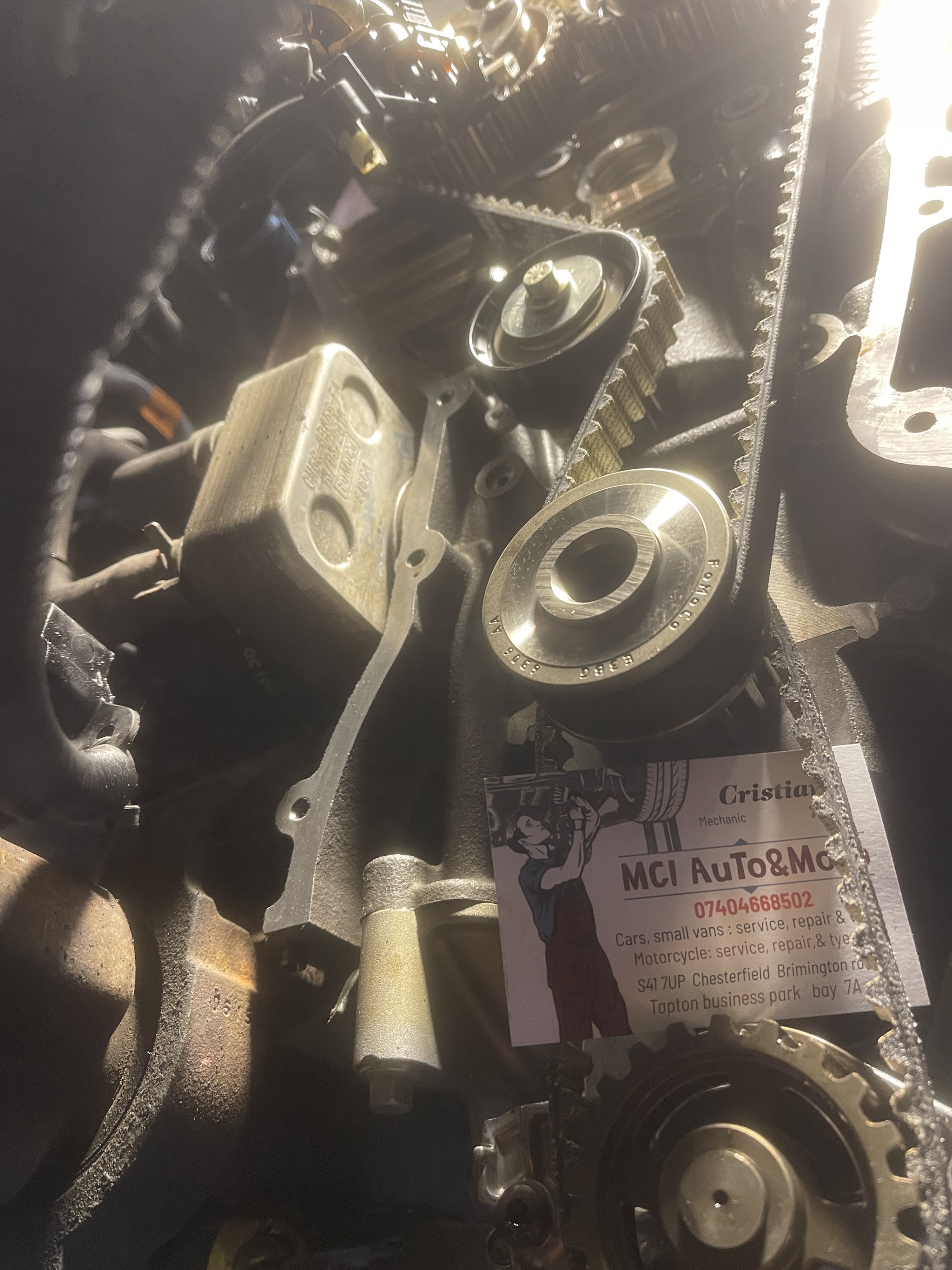 Timing belt and tensioner job under the workshop lights, with the MCI AuTo&MoTo business card on the engine